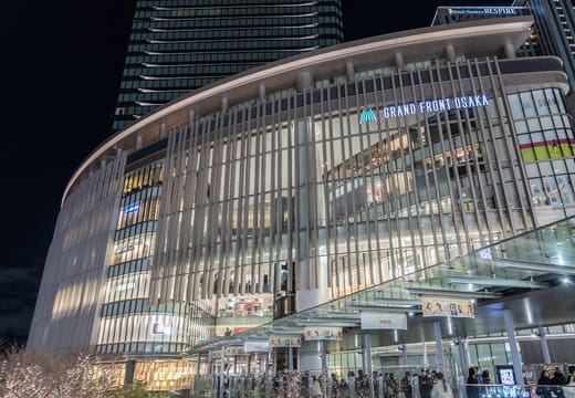 Curved glass and white fins of Grand Front Osaka lit up at night
