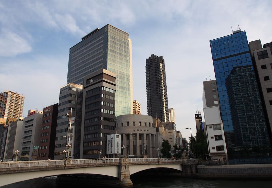 Round Osaka Exchange Building beside a bridge among office towers