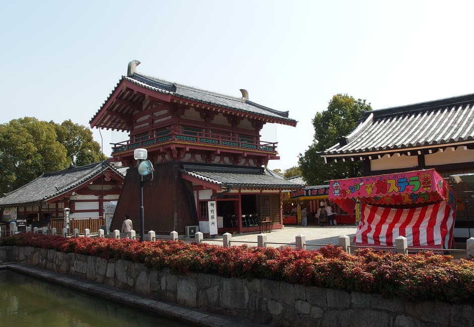 Five-storey pagoda and halls of Shitenno-ji behind a pond with flower beds